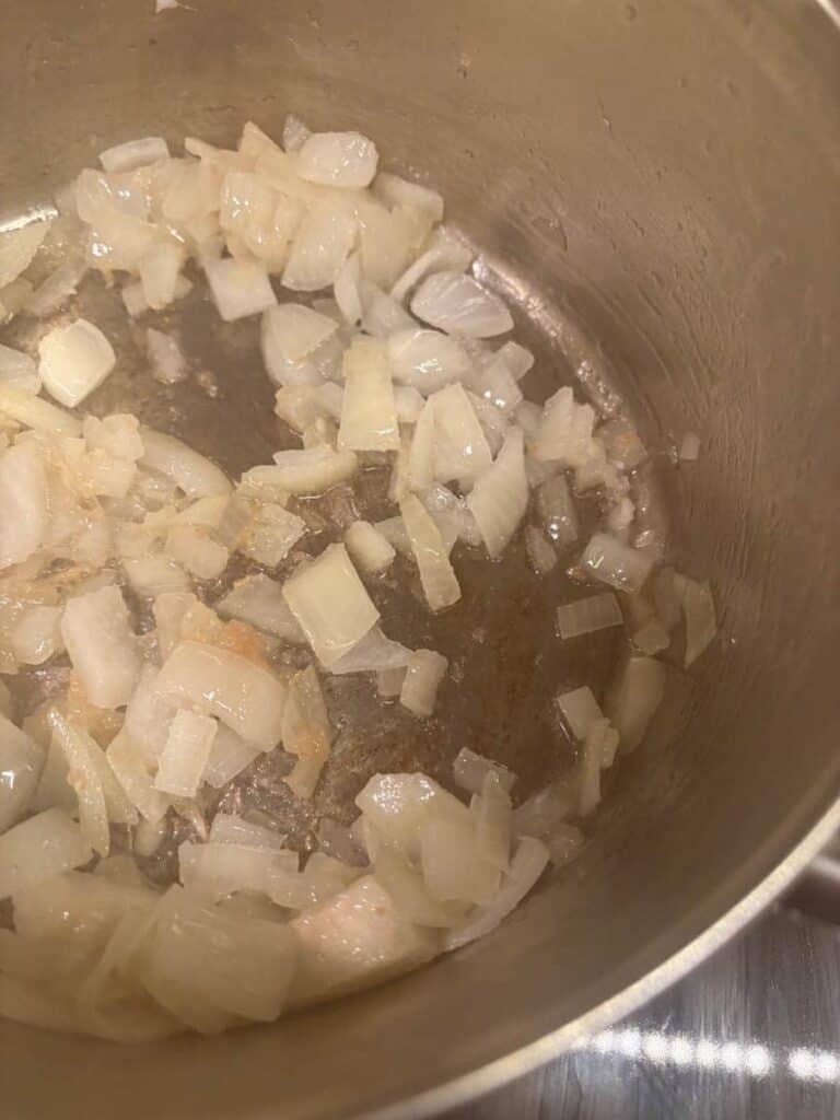 Diced onions cooking in oil in a silver saucepan.