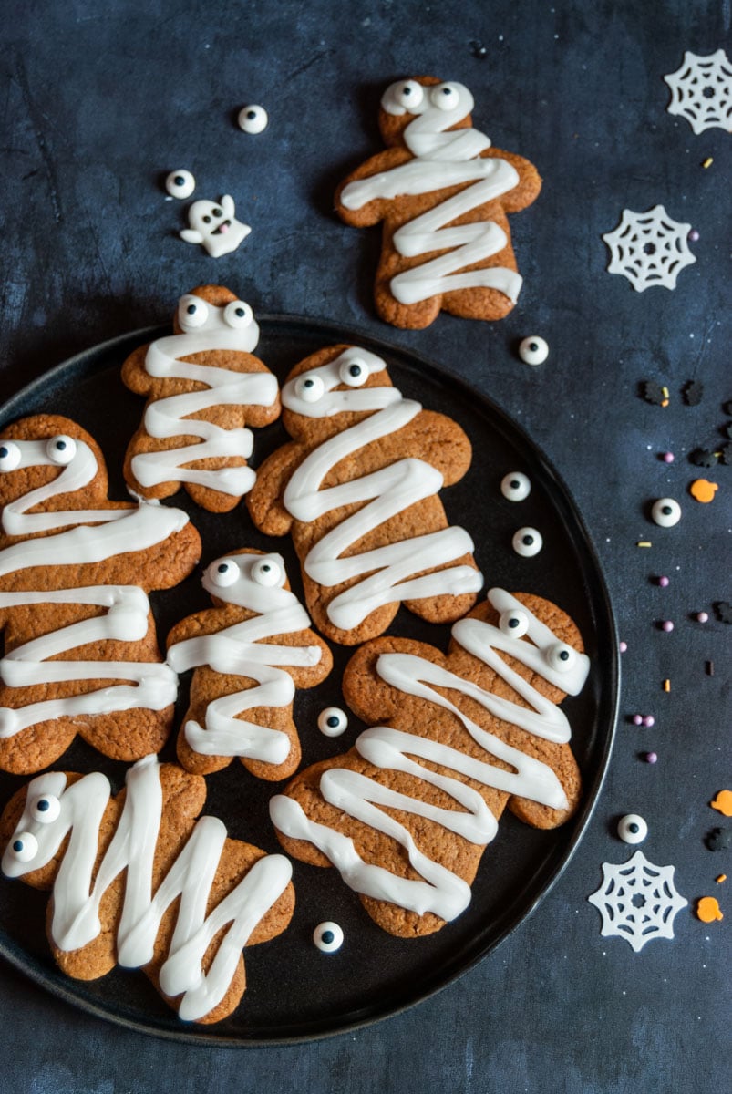 gingerbread cookies with white icing and candy eyes on a black plate.