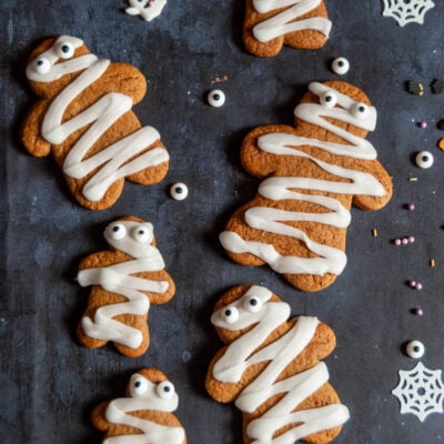 six gingerbread cookies decorated with white icing and candy eyes.