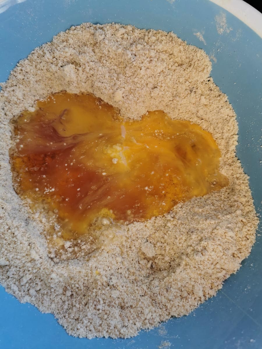 Golden syrup and a beaten egg being mixed into flour and butter.