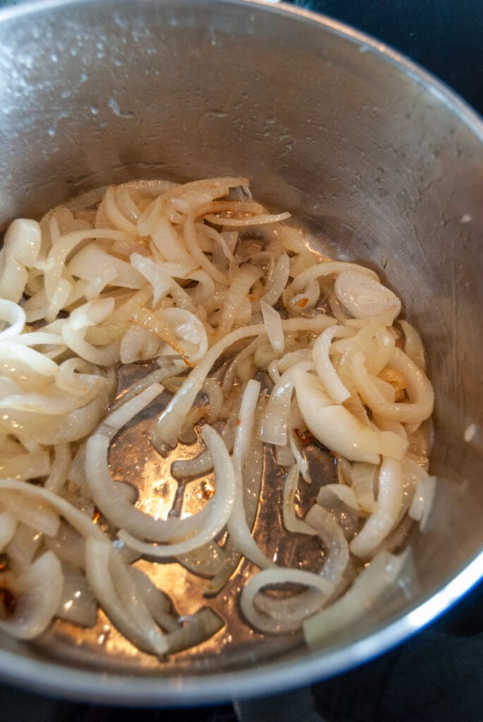 Sliced onions cooking in a silver pan.