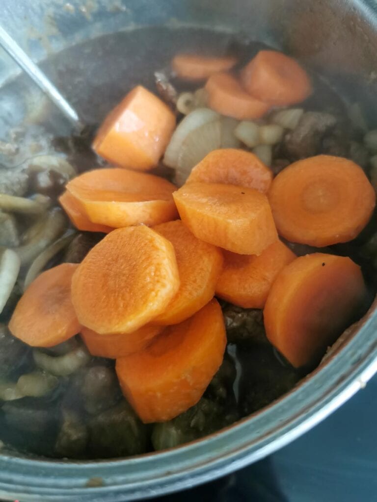 beef, onions and carrots in a saucepan with gravy.