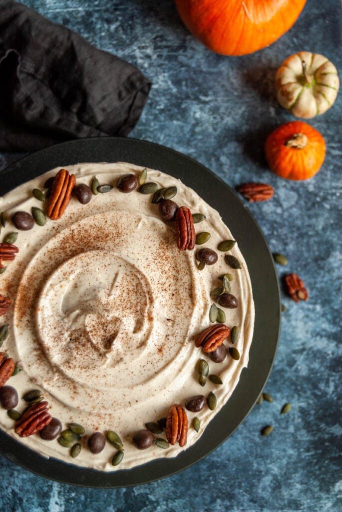 an overhead photo of a pumpkin spice layer cake decorated with pecan nuts, pumpkin seeds and chocolate covered coffee beans on a black plate,