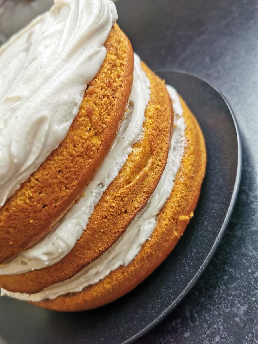 Three layers of pumpkin sponge cake with cream cheese frosting on a black plate