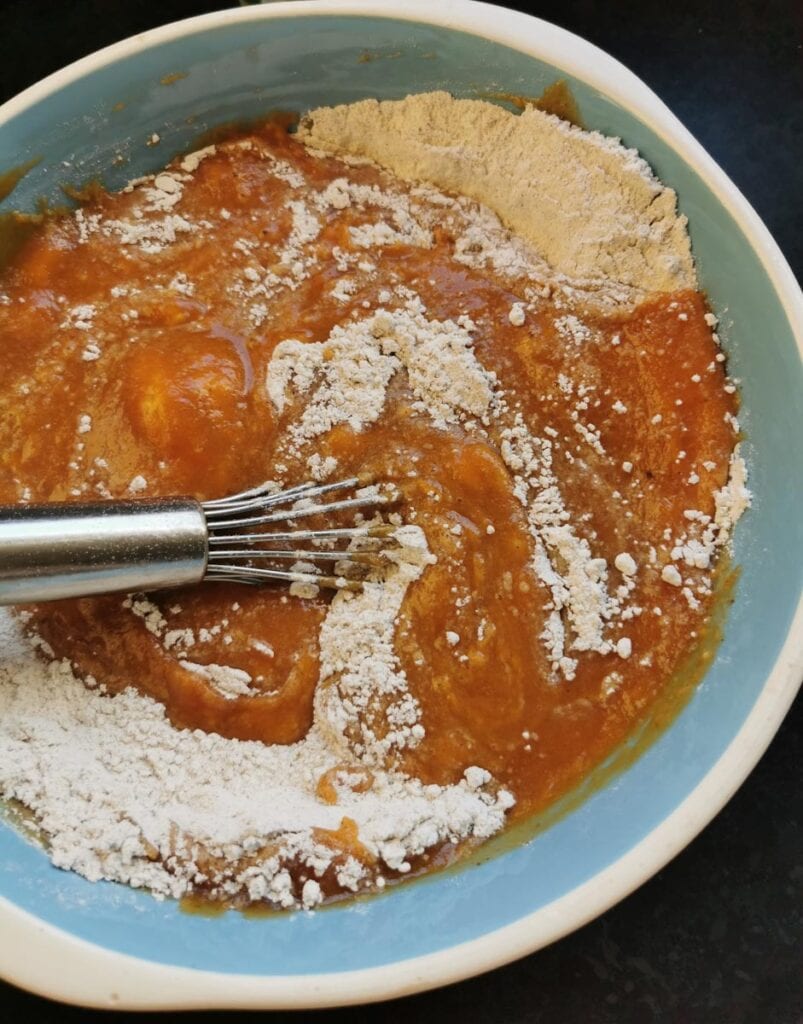 A bowl of pumpkin purree, oil, eggs and flour with a whisk.
