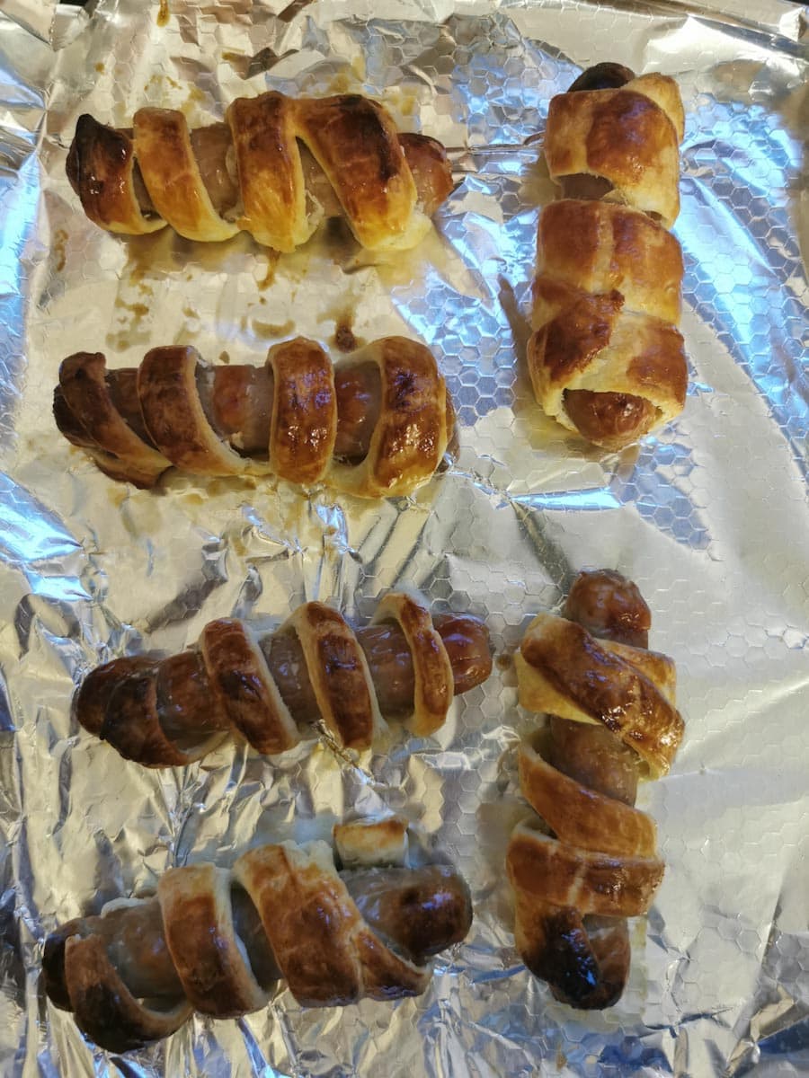 six Puff pastry wrapped sausages on a foil covered tray.