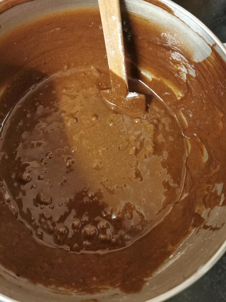 A large silver bowl of brownie batter with a wooden spatula