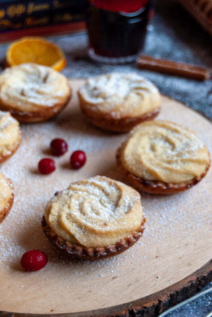 mince pies topped with a viennese shortbread swirl on a wooden board with fresh cranberries.