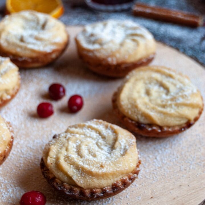 mince pies topped with a viennese shortbread swirl on a wooden board with fresh cranberries.