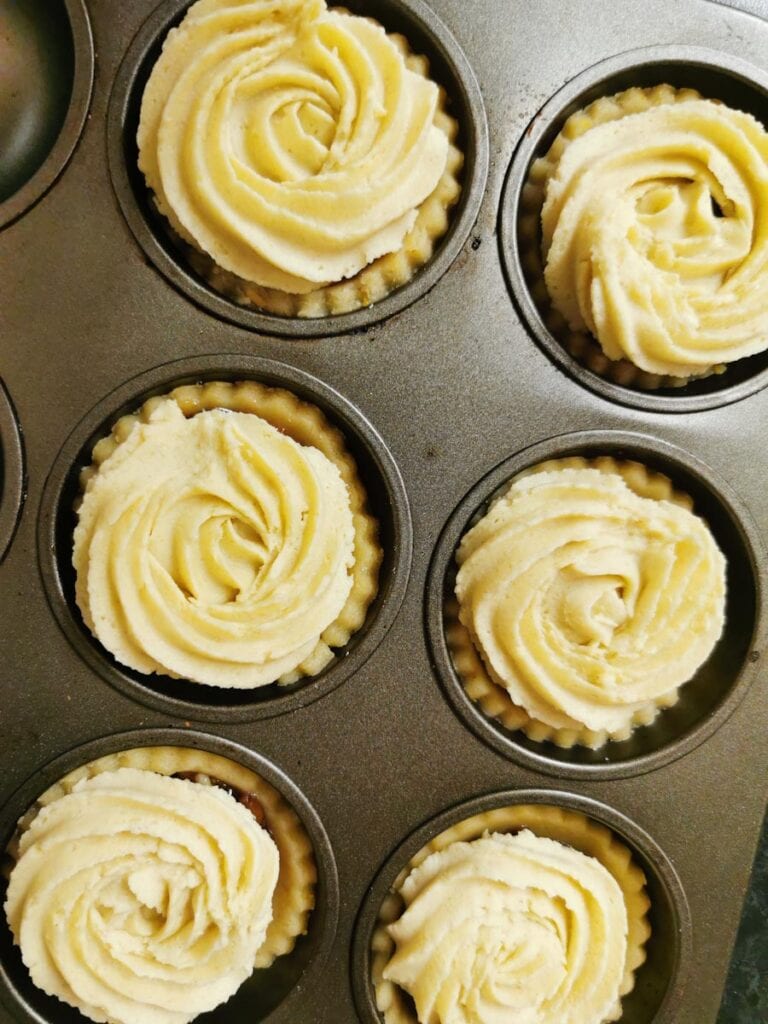a silver baking tin of unbaked mince pies with a Viennese whirl topping.