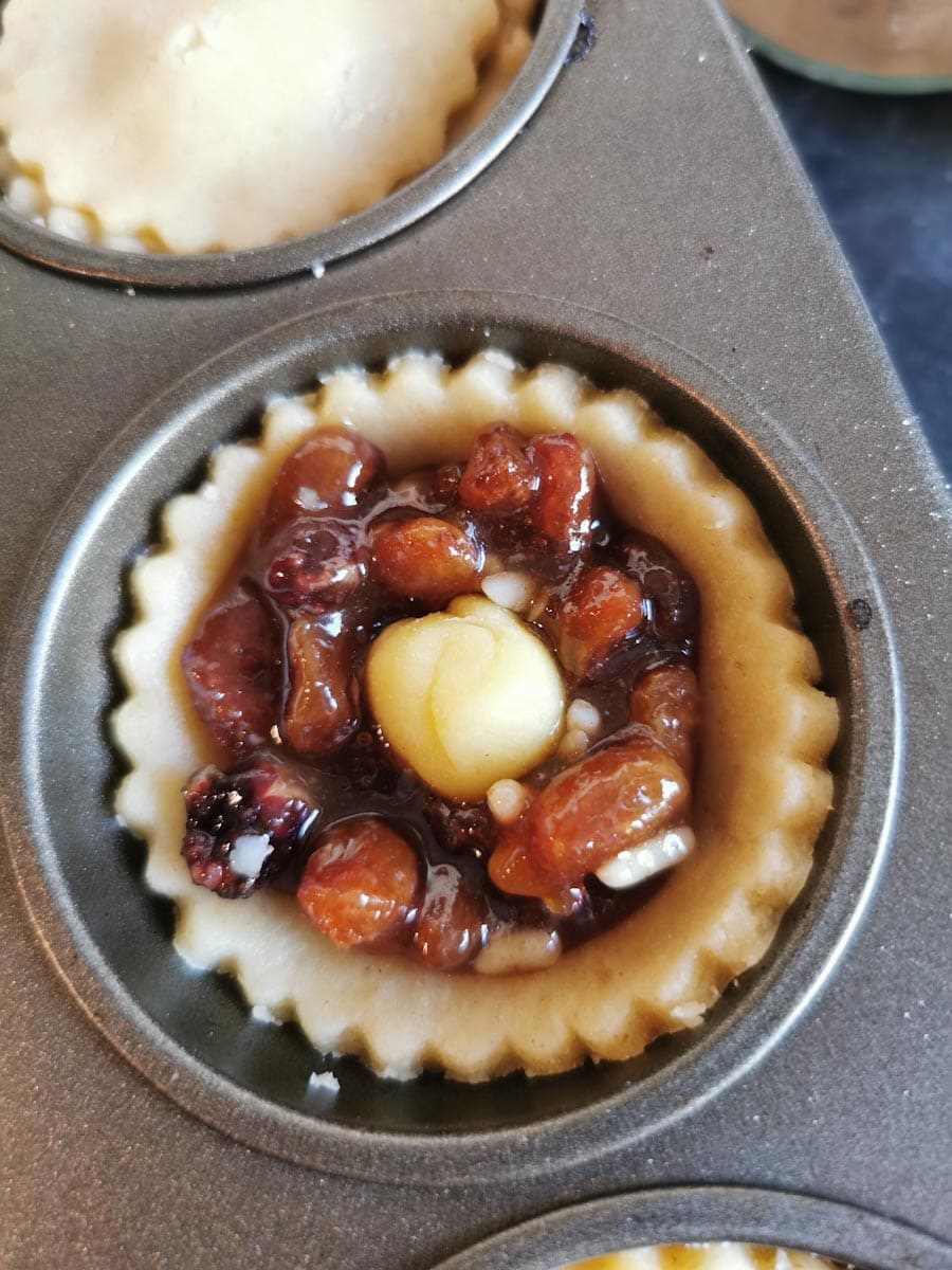 a close up picture of a baking tin lined with pastry and filled with mincemeat and a small piece of marzipan.