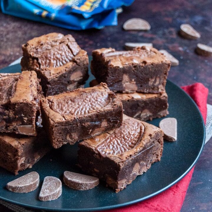 a black plate of chocolate brownies with milk chocolate orange chunks and a packet and Terrys chocolate orange segments.