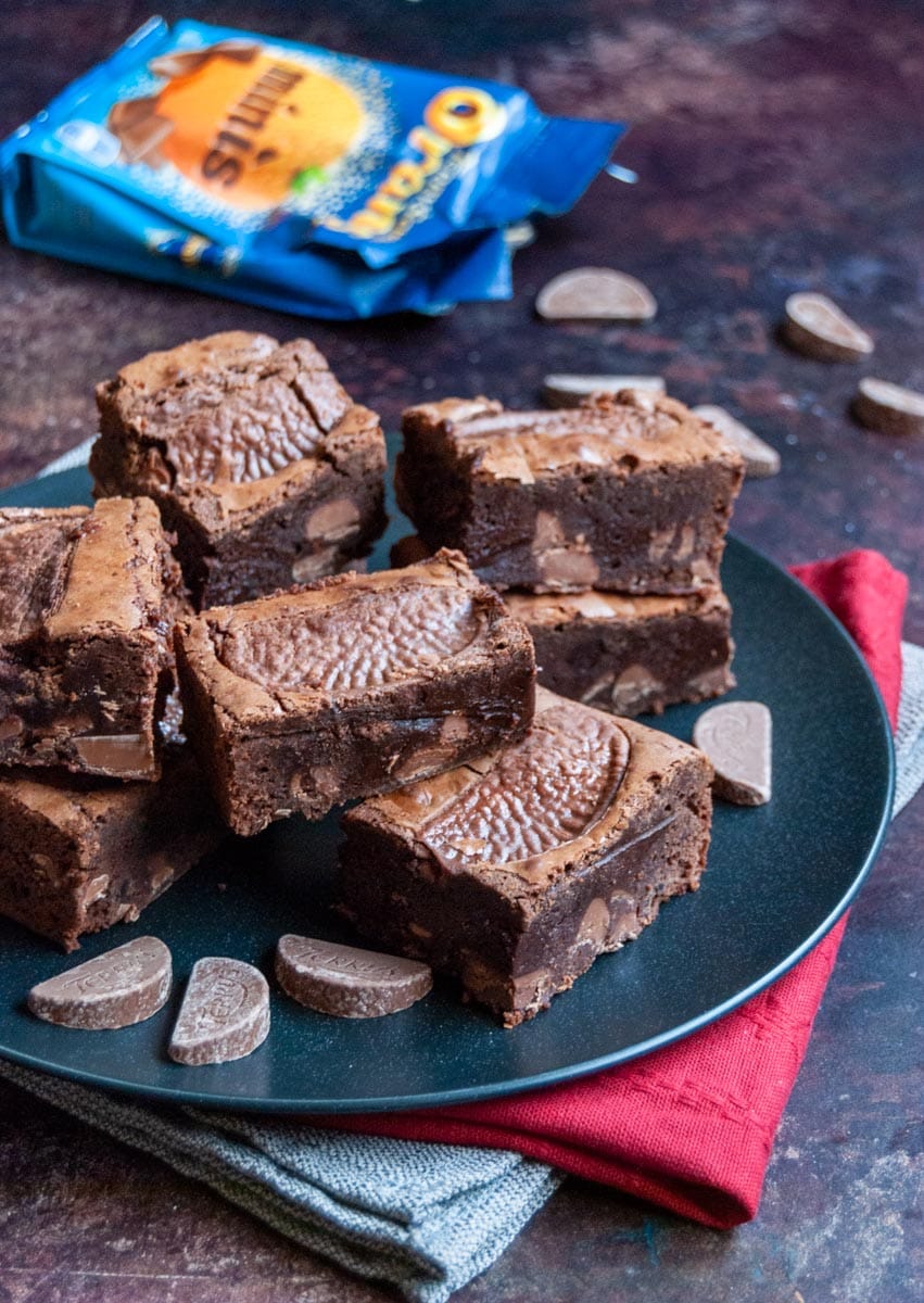 a black plate of chocolate brownies with milk chocolate orange chunks and a packet and Terrys chocolate orange segments.