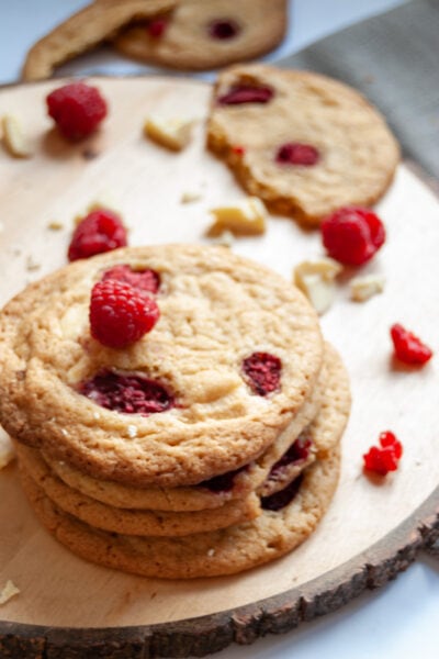 a stack of white chocolate cookies with raspberries on a wooden serving board.