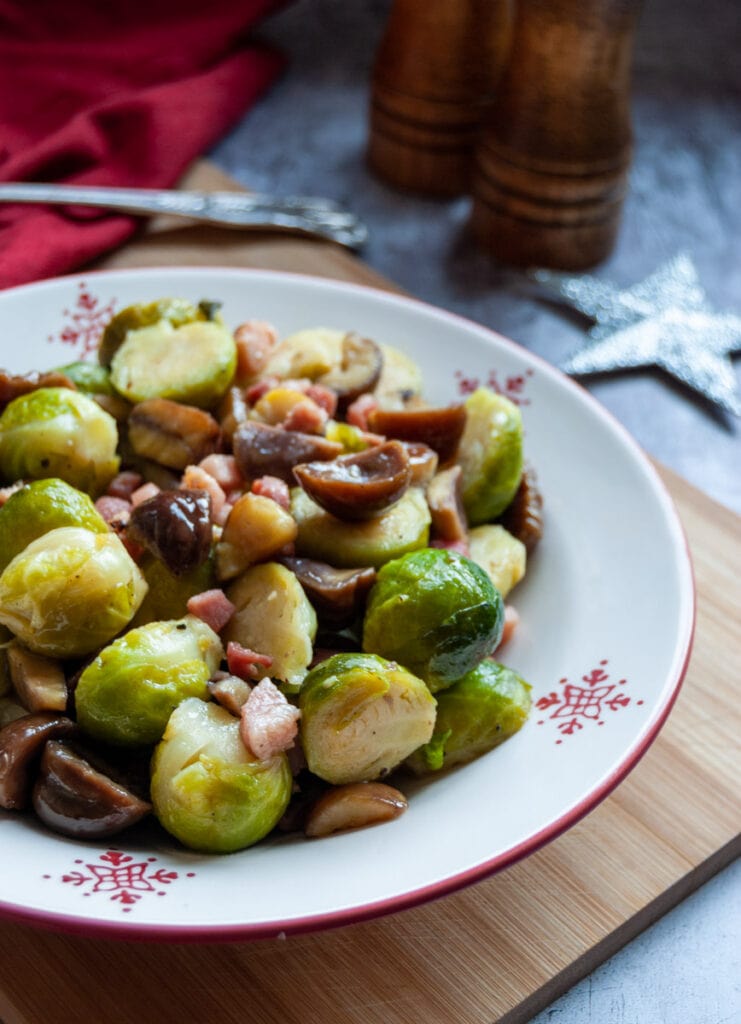 a red and white bowl of sprouts with pancetta cubes and chestnuts, a silver star decoration and a wooden salt and pepper mill