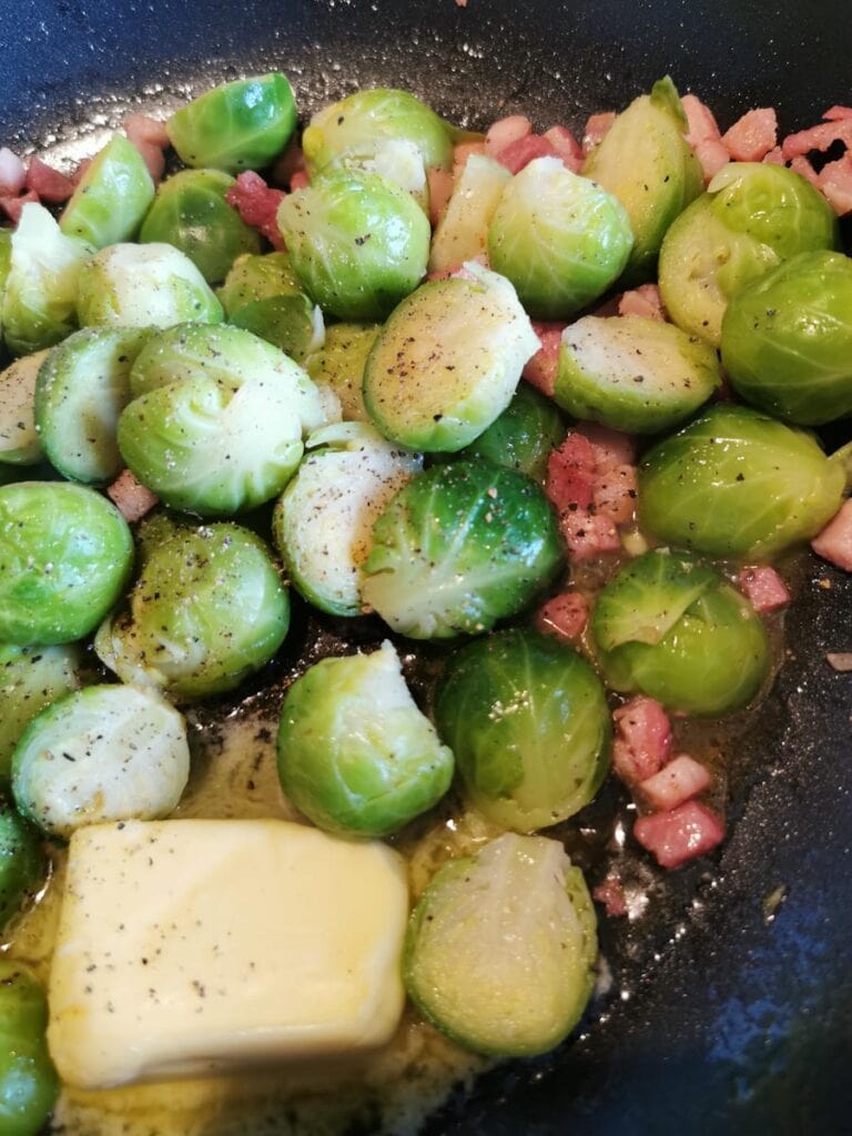 brussels sprouts frying in a pan with bacon and butter