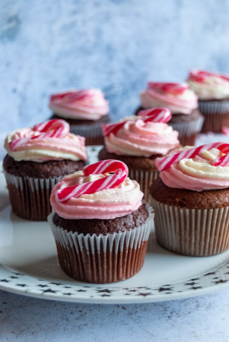 a batch of chocolate cupcakes topped with peppermint frosting and a mini candy cane on a white and gold star plate.