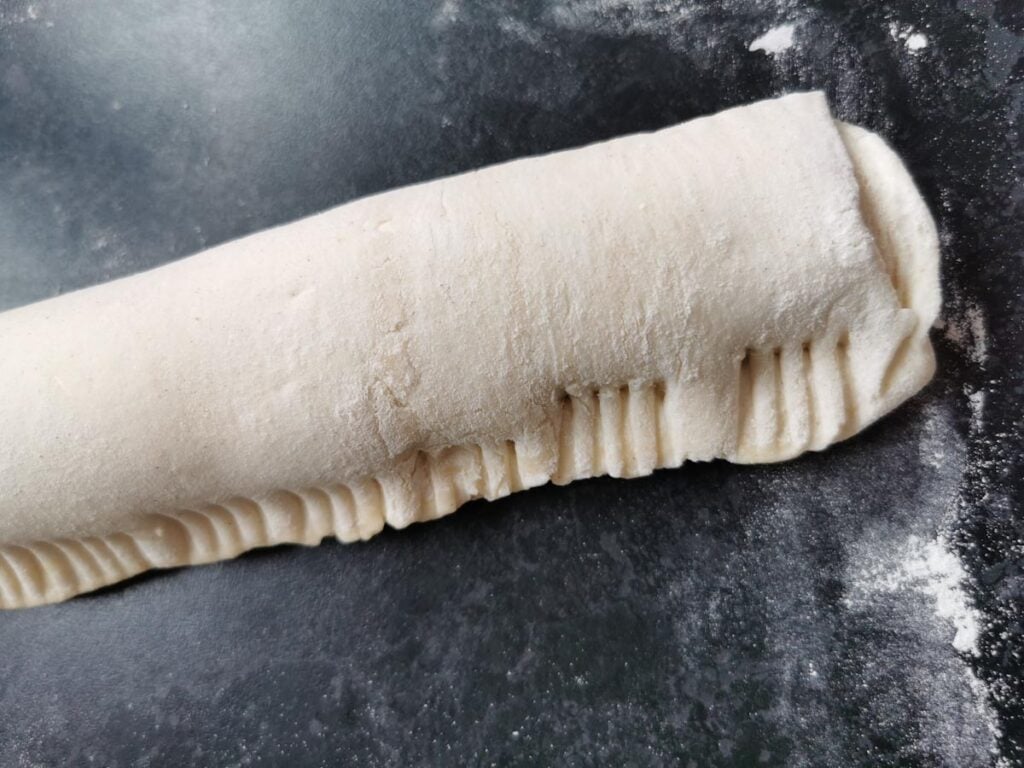 A long unbaked sausage roll. The edges of the pastry have been crimped with a fork.