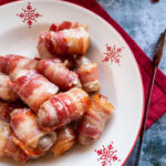 a red and white Christmas bowl of little sausages wrapped in bacon on a red napkin.