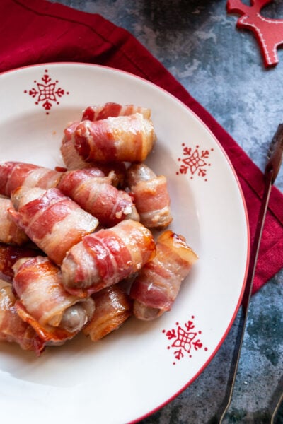 a red and white Christmas bowl of little sausages wrapped in bacon on a red napkin.