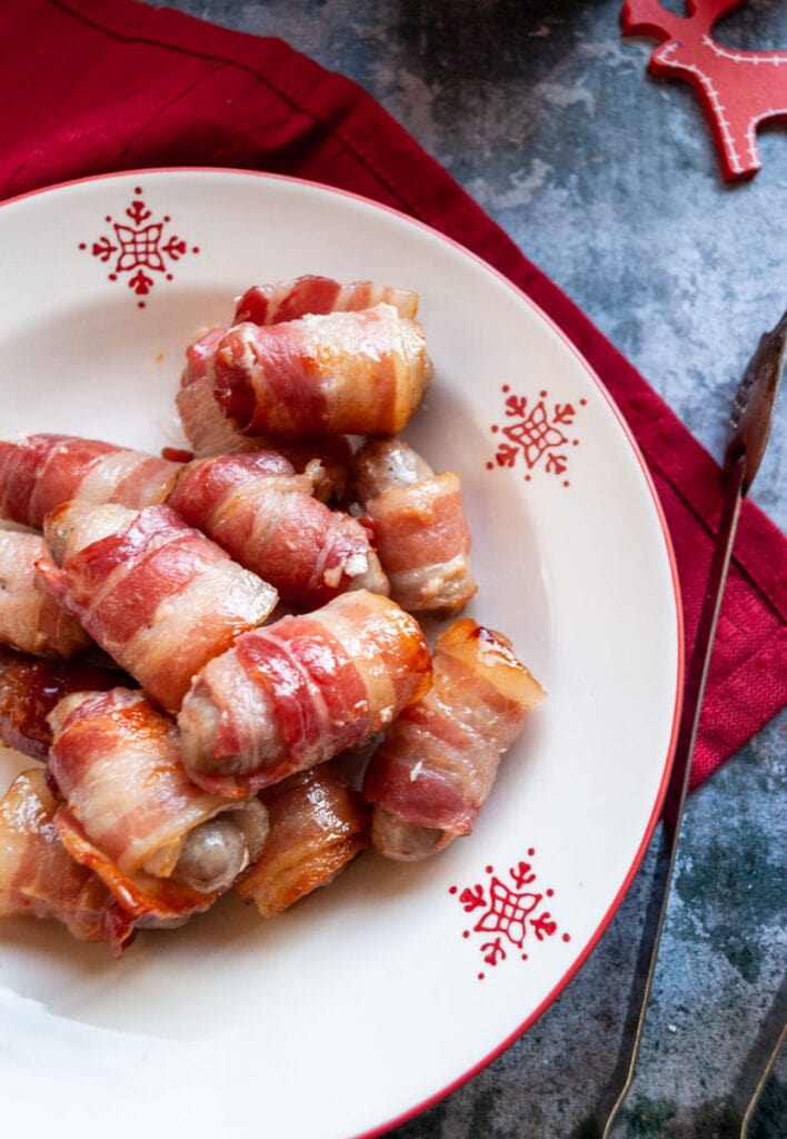 a red and white Christmas bowl of little sausages wrapped in bacon on a red napkin.