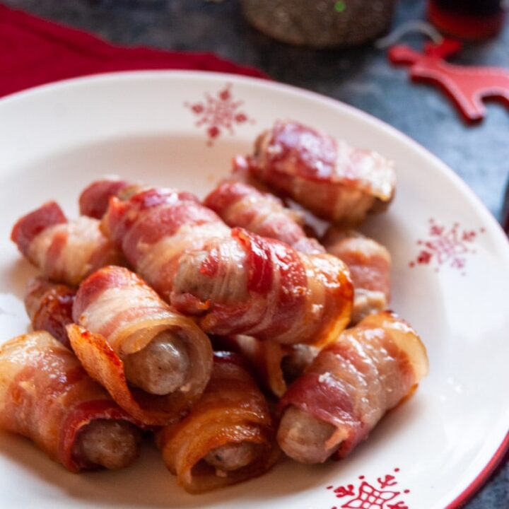 a red and white Christmas bowl of little sausages wrapped in bacon.