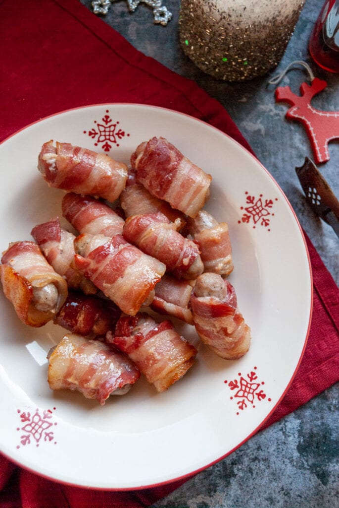 a red and white bowl of bacon wrapped sausages.