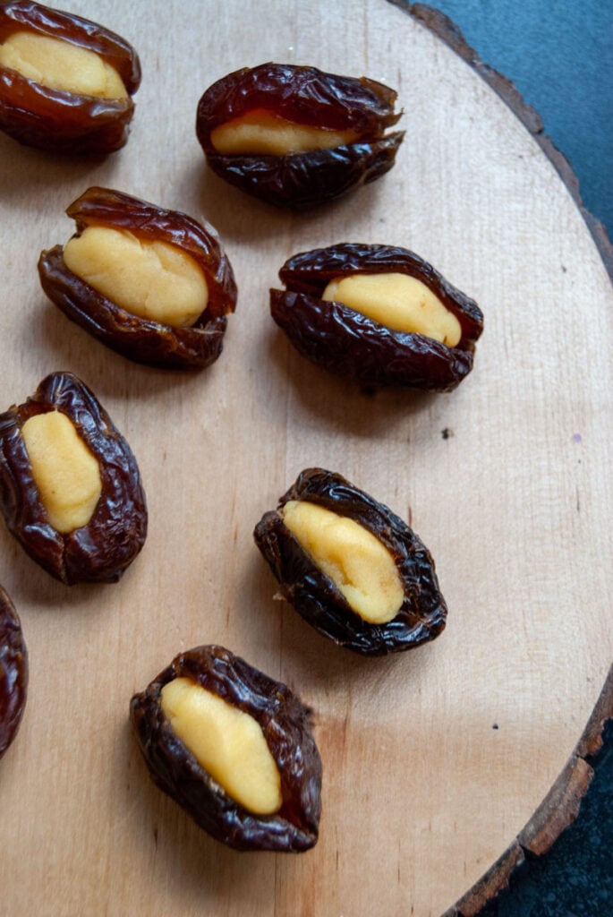 Medjool dates stuffed with yellow marzipan on a wooden board.