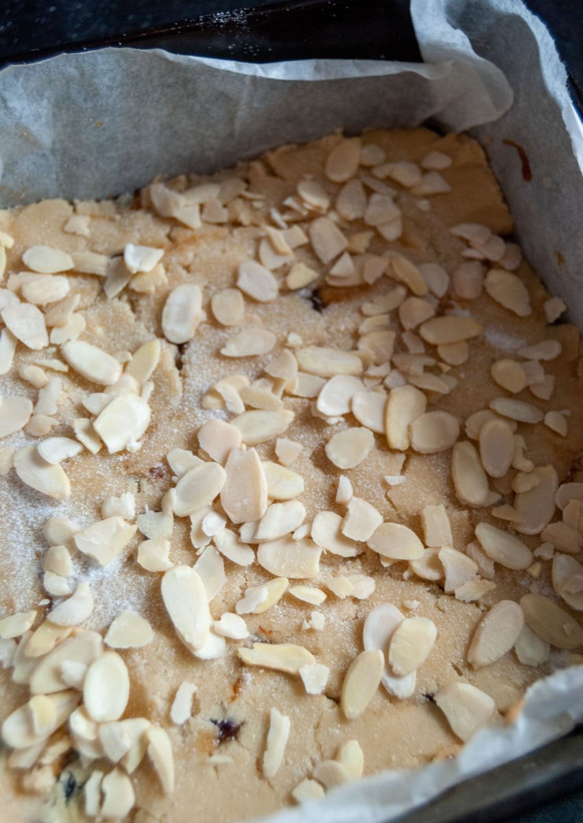 unbaked shortbread filled with mincemeat and sprinkled with caster sugar and flaked almonds in a square bakking tin.
