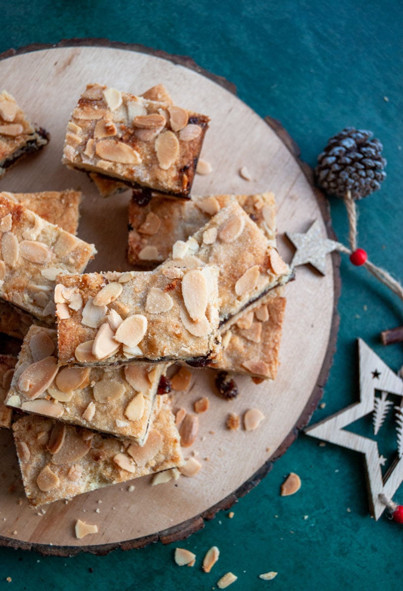 mincemeat filled shortbread bars topped with flaked almonds on a wooden serving board and dark green backdrop with a wooden star Christmas decoration