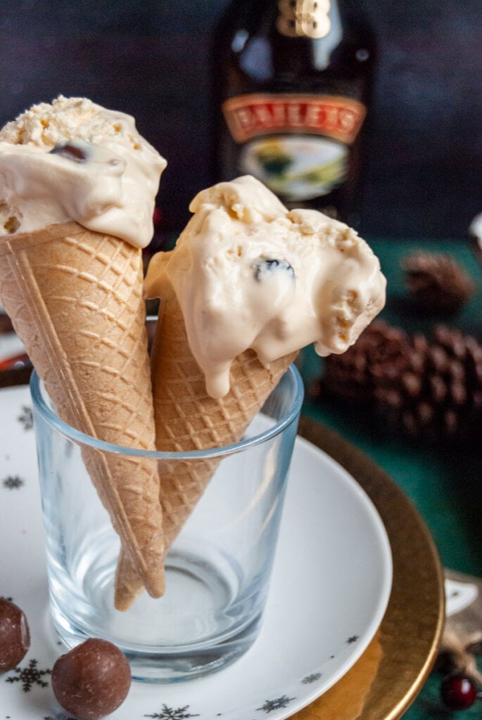 two ice cream wafer cones sitting in a small glass filled with Baileys flavoured ice cream. A bottle of Baileys and pine cones can be seen in the background.