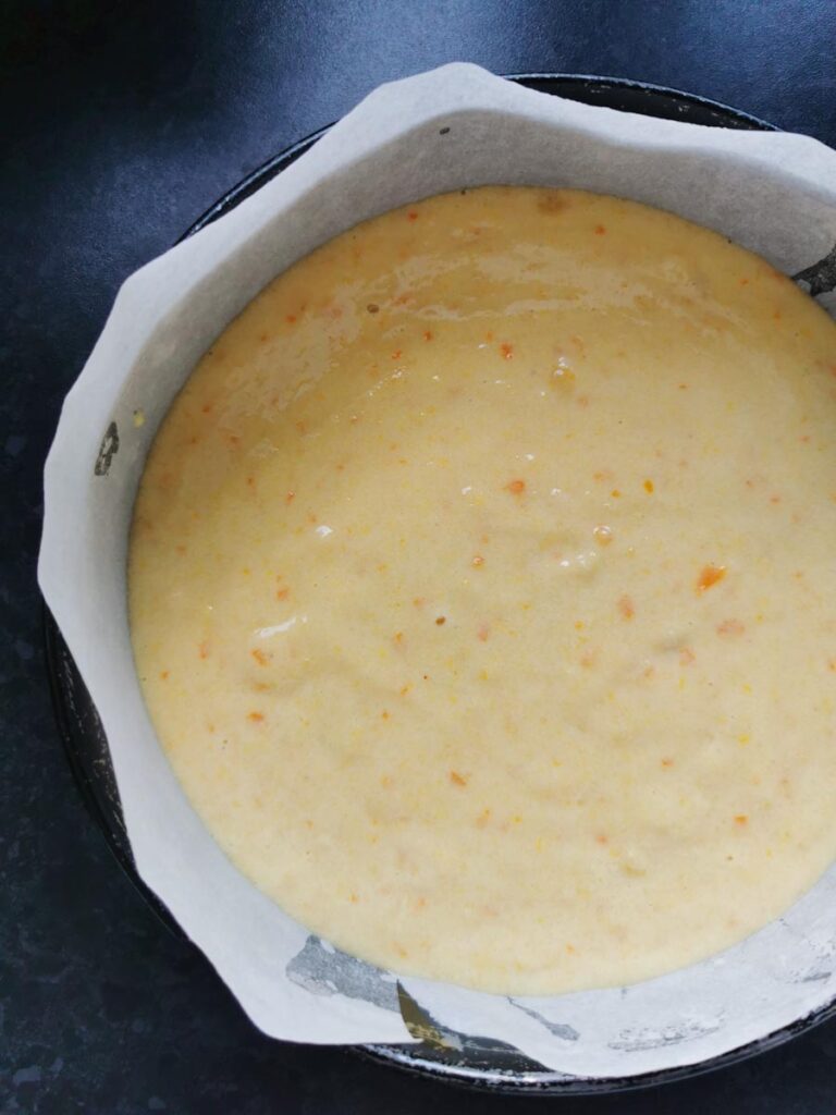 an unbaked orange cake in a round cake tin lined with baking paper.