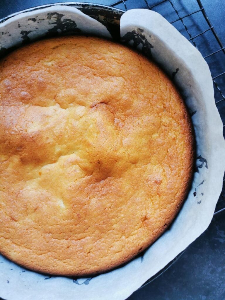 a freshly baked orange cake in a round cake tin lined with baking paper.