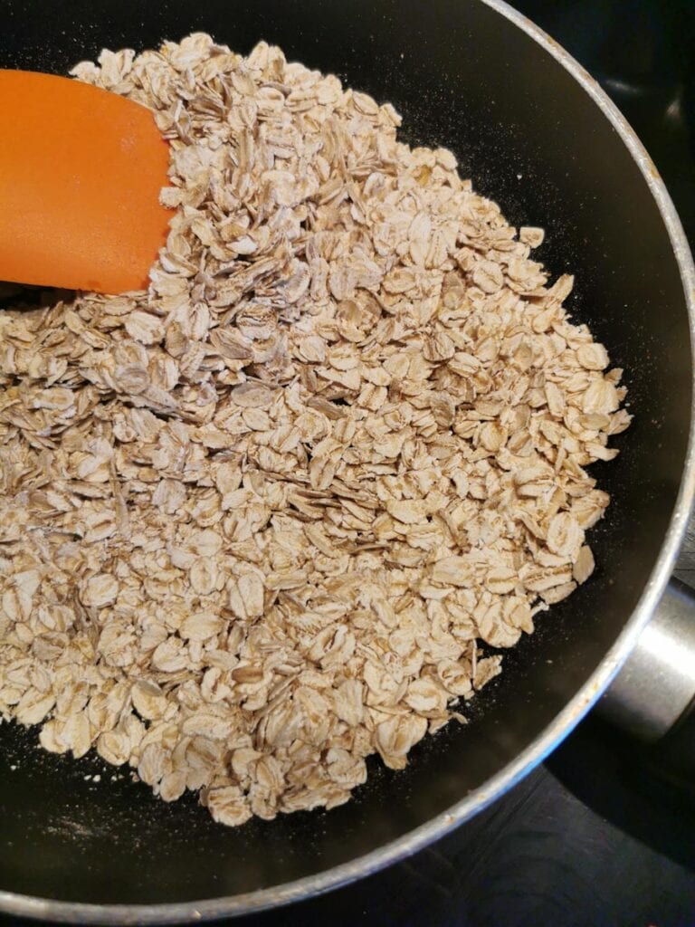 rolled oats in a frying pan with an orange spatula.