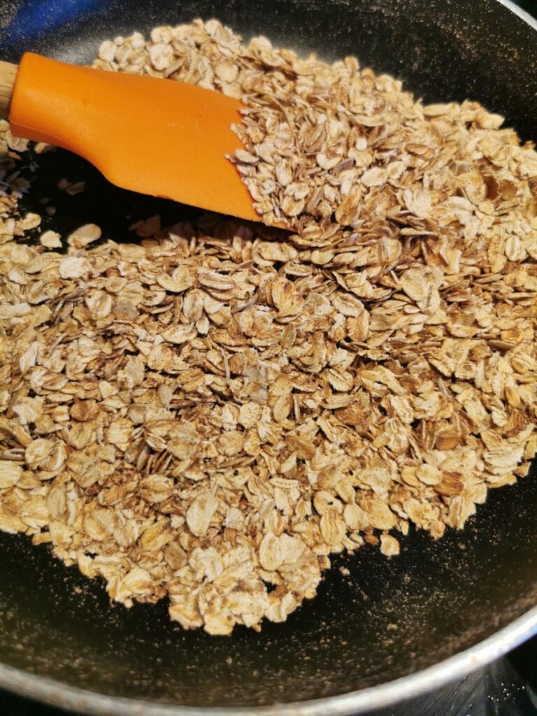 toasted oats in a frying pan with a wooden spatula.