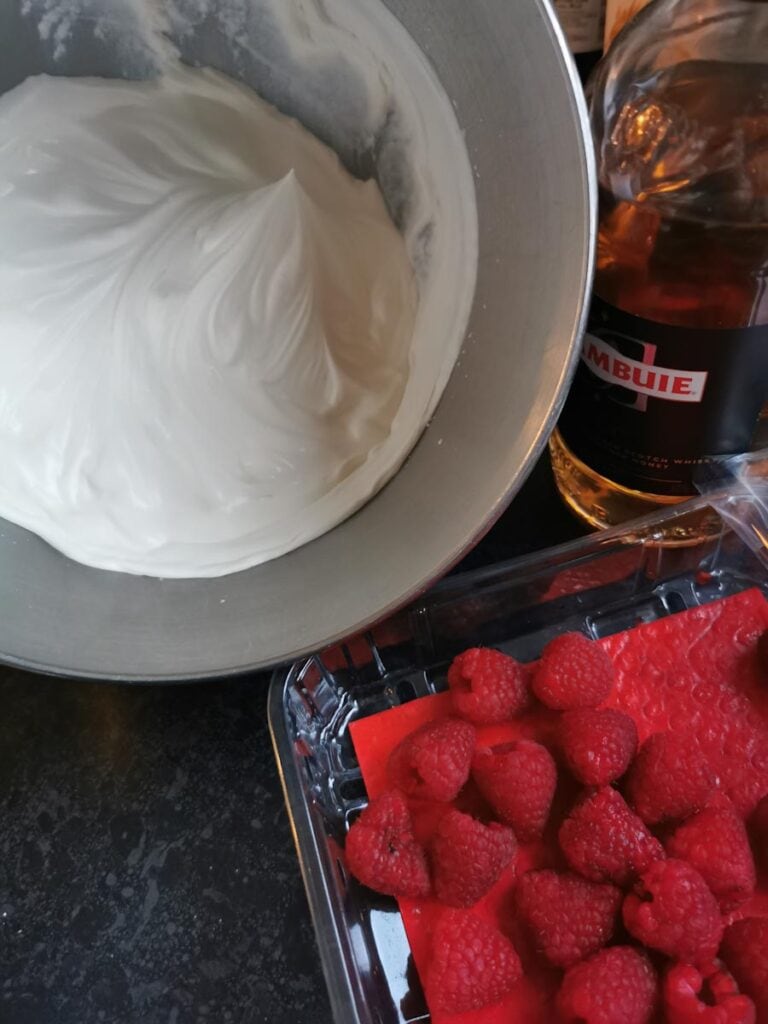 a silver bowl of whipped cream, a bottle of Drambuie and a box of fresh raspberries.