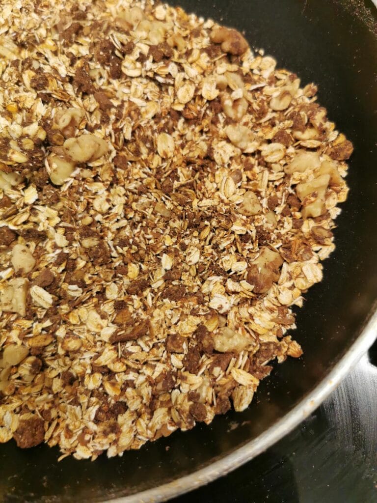 toasted oats and chopped walnuts in a frying pan with a wooden spatula.