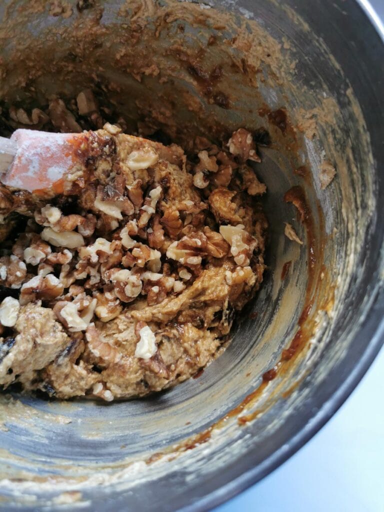 walnuts being stirred into a silver bowl of date and walnut cake batter.