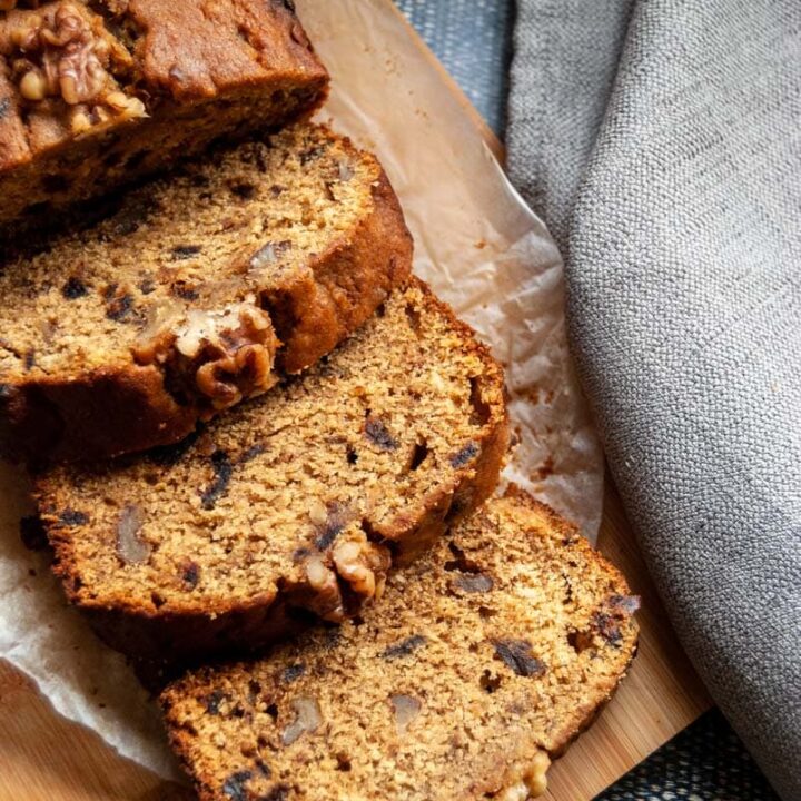 a partially sliced date and walnut loaf on a wooden chopping board with a grey linen napkin.