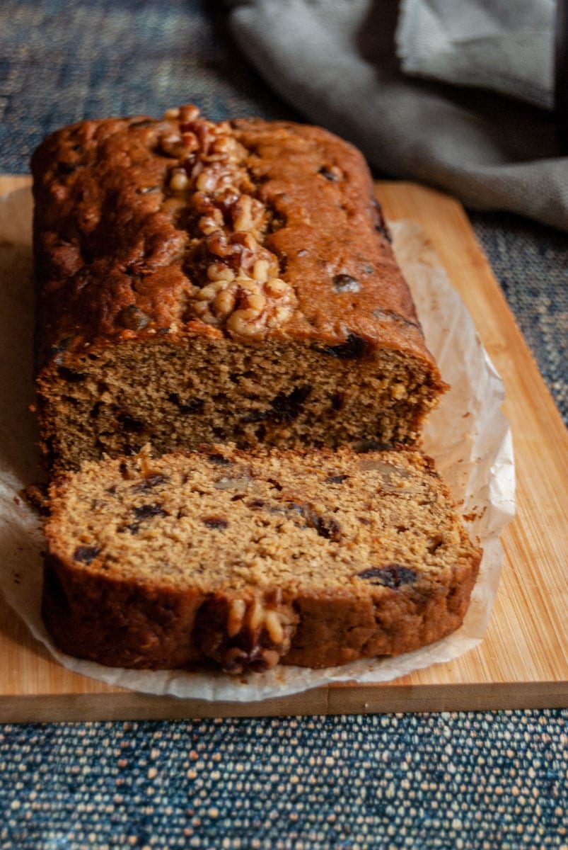 a date and walnut loaf cake on a wooden chopping board and a grey napkin.