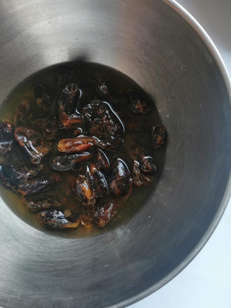 a silver bowl of dates soaking in hot water.