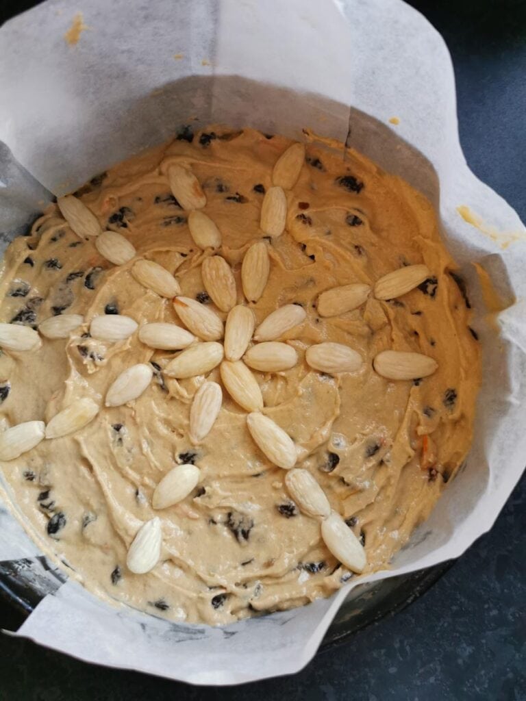 fruit cake batter topped with blanched almonds in a lined round cake tin.