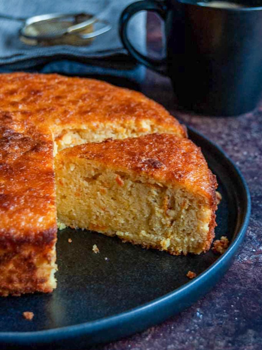 an orange cake on a black plate with a black mug and grey napkins.