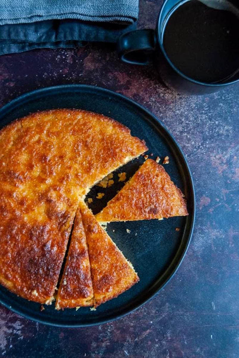 an orange cake with a slice cut out of it on a black serving plate.