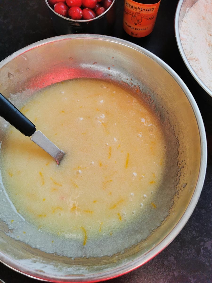 a silver bowl of orange cake batter with a black handled fork.