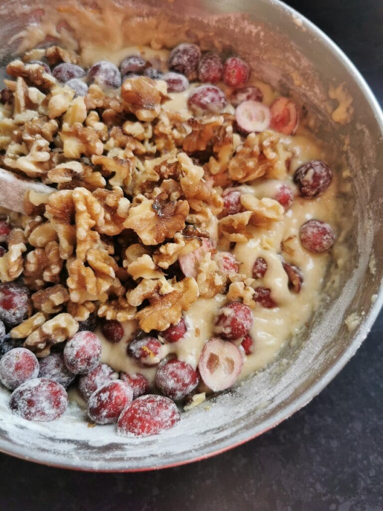 Walnuts and fresh cranberries being folded into a silver bowl of cake batter.
