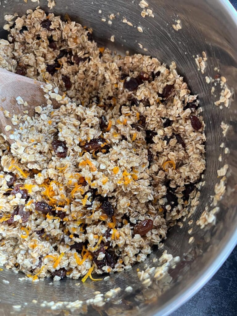 a silver bowl of oats, sultanas and orange zest coated in melted butter and syrup to make flapjacks.