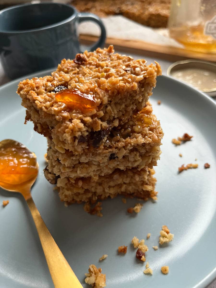 three flapjack bars with sultanas and glazed with orange marmalade and a gold spoonful of marmalade on a blue plate.