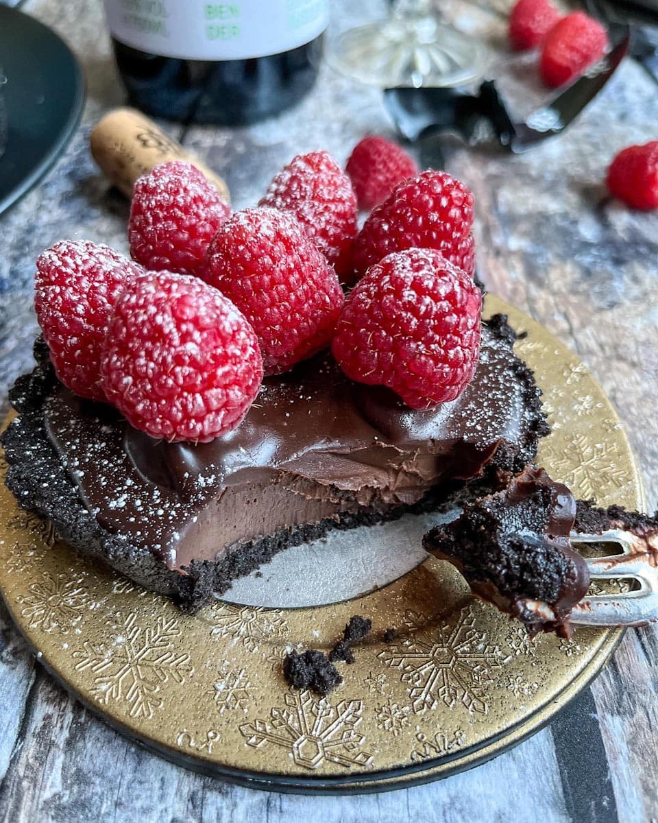 a mini chocolate ganache tart topped with fresh raspberries on a small gold plate.
