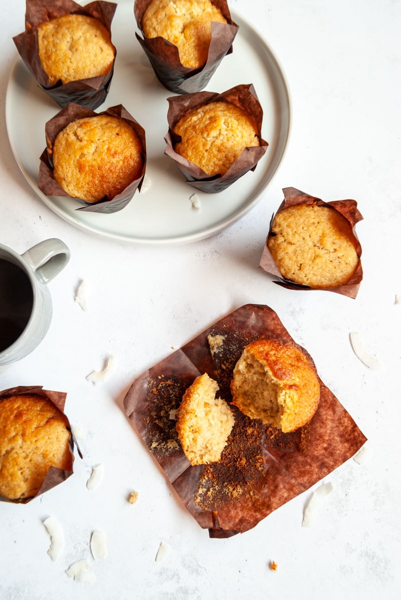 Banana muffins in brown paper liners on a white background and plate with a cup of coffee.